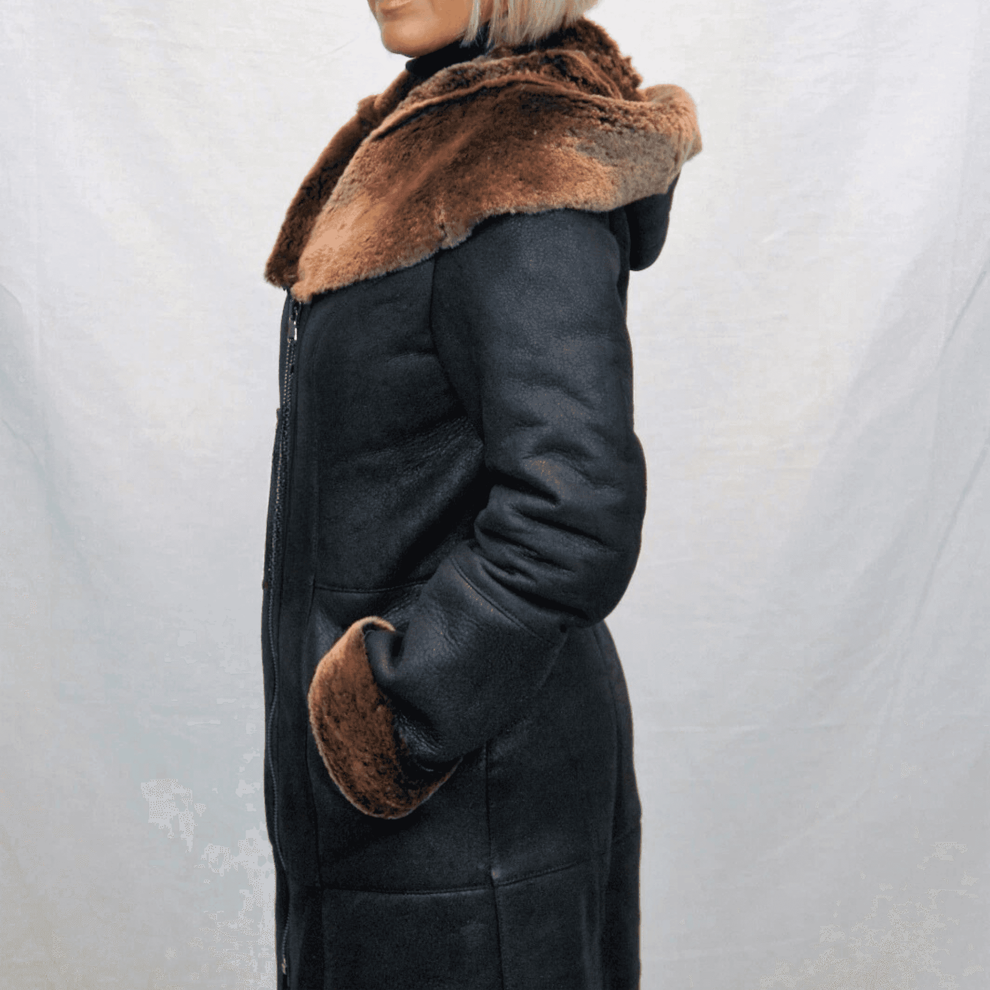 Side profile of woman wearing a long black Sheepskin Shearling Coat with brown fur lined hood and cuffs